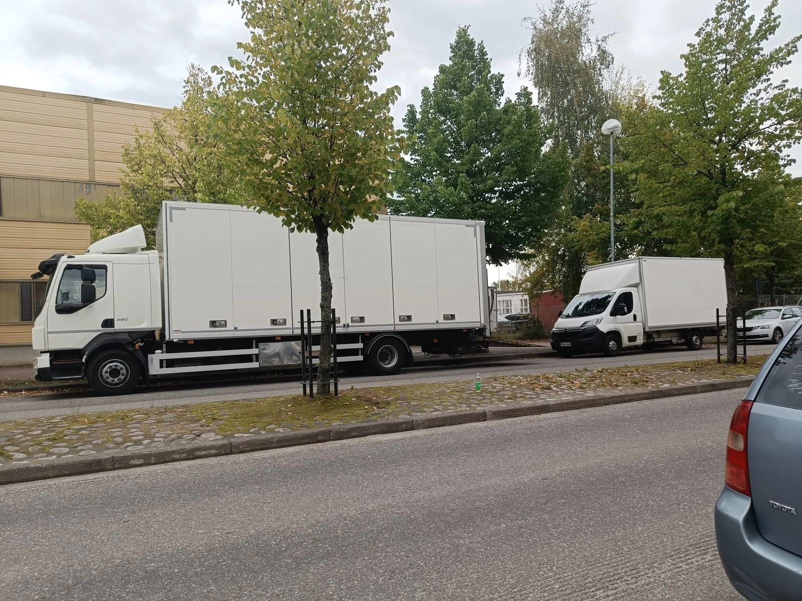 Kaksi valkoista muuttoautoa pysäköitynä kadun varteen.